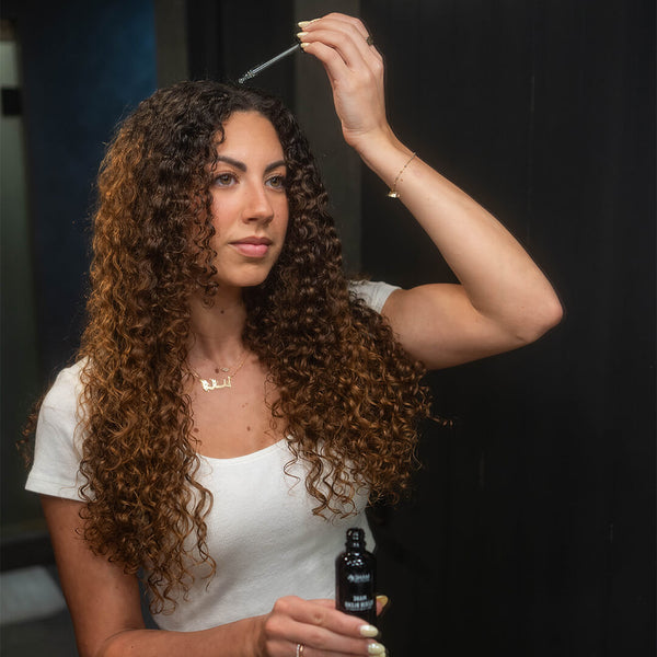 Woman applying Mane Elixir Blend hair growth oil to her curly hair, demonstrating the product's use for enhancing hair growth.